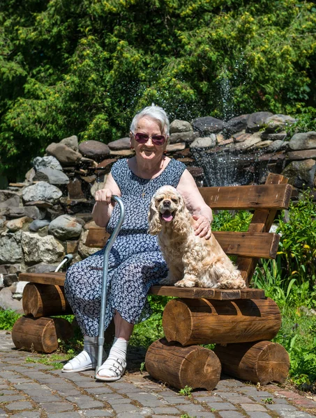 Vieille femme assise sur un banc avec un chien — Photo