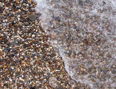 Deniz sahilinde çakıl taşları. Köpükle dalgalanan dalgalar