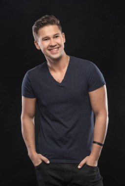 Stüdyoda siyah arka planda poz veren gülümseyen yakışıklı adamın portresi.