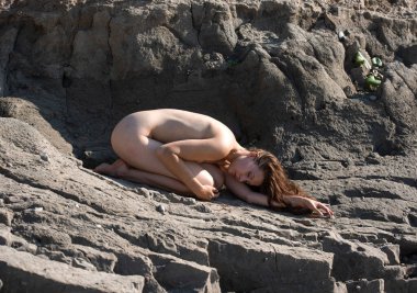 Plajda çatlak bir toprak üzerinde poz veren çıplak bir kadın. Seksi esmer, güneşlenen ve sıcak yaz gününün tadını çıkaran.