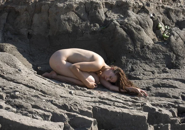 Plajda çatlak bir toprak üzerinde poz veren çıplak bir kadın. Seksi esmer, güneşlenen ve sıcak yaz gününün tadını çıkaran.