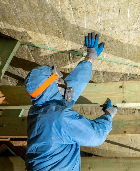 Attic renovation and insulation concept. Worker in uniform installing thermal roof insulation layer using mineral wool panels