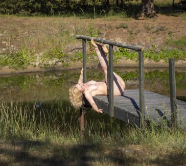 Küçük bir köprüde poz veren çıplak bir kadın. Seksi sarışın Sıcak yaz gününün tadını çıkarıyor 