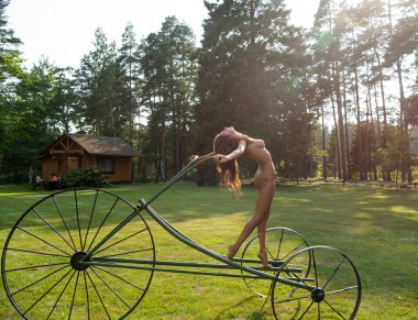 Genç çıplak kadın yaz tatilinin tadını çıkarıyor. Sıcak güneşli bir günde dekoratif bisiklette poz veren seksi esmer.