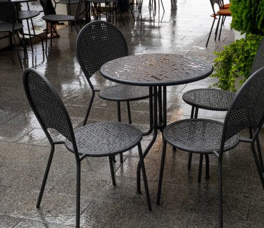 Yağmurdan ıslanmış bir sokak kafesinin masa ve sandalyeleri.