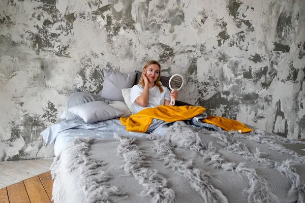 Mladá žena obdivuje sama sebe v zrcadle, zatímco v posteli Royalty Free Stock Obrázky