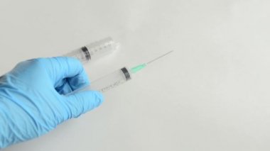 Doktor beyaz yüzeye bir şırınga koyup Coronavirus aşısı için eldiven takıyor.