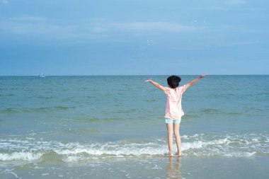 Asyalı kızın arkadan görünüşü deniz manzarasına bakar ve sahile su sıçratır.