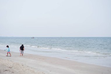 Denizde yüzen balıkçı teknesi ve plajda oynayan küçük kız ve oğlanın bulanık ön planı.