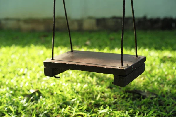 Arka bahçedeki ağaçtan sarkan eski ahşap salıncak.