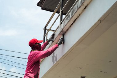 Side view of worker removing the old color out of the surface of the cement wall
