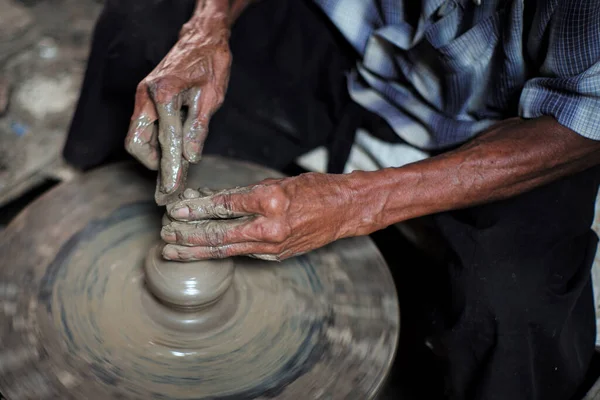 Selective focused on the dirty wrinkled skin hands of old man molding the clay work on the spinning wheel for making the traditional jar