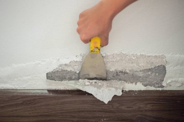 Beton duvarın su toplamış yüzeyine odaklanın. Duvardan tabloyu kaldıran işçinin bulanık eliyle nemden şişmiş renkli duvar.