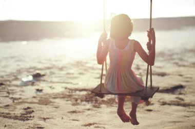 Yalnız Asyalı kızın arkadan görünüşü ahşap salıncakta oturur ve arka planda günbatımı vardır.