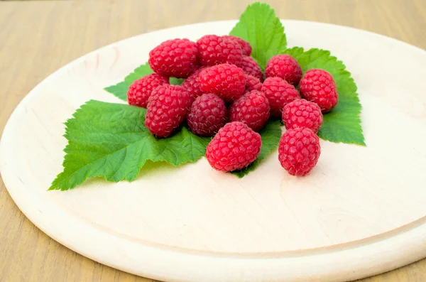 Raspberries are on a round wooden board — Stock Photo, Image