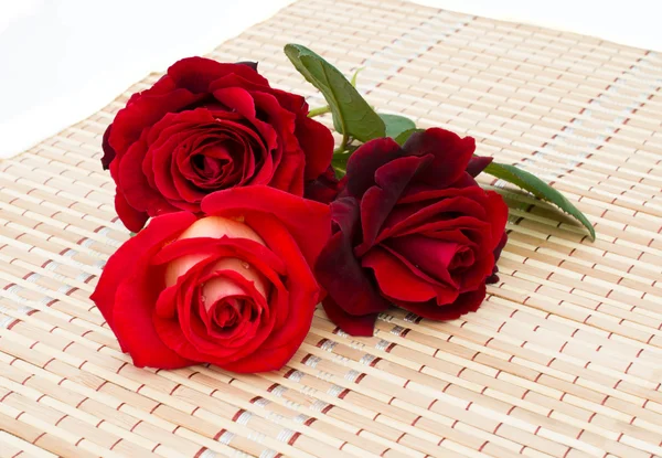 Three red roses are on a bamboo napkin — Stock Photo, Image