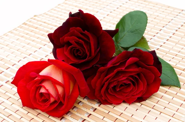 Three red roses are on a bamboo napkin — Stock Photo, Image