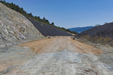 Construction site of an expressway through a rural area with a cut in the hill. The cut is lined with anti-slide netting.