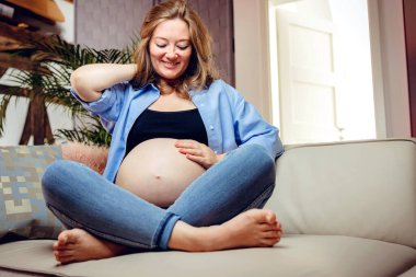 pregnant woman sitting on sofa and looking at her belly 