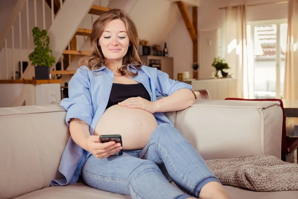 Pregnant Woman Using Mobile Phone While Sitting Sofa Home — Stockfoto