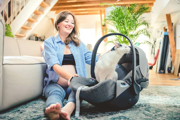 young woman with a baby car seat sitting with her cat on the floor at home