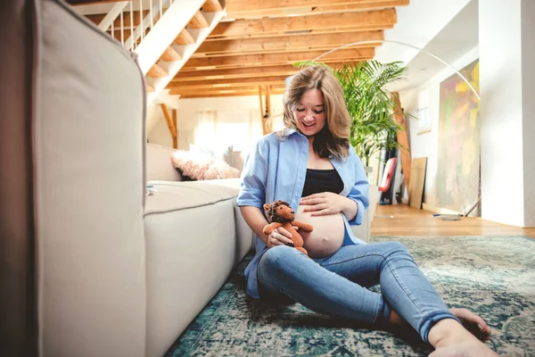 portrait of a pregnant woman with toy lion sitting on the floor at home