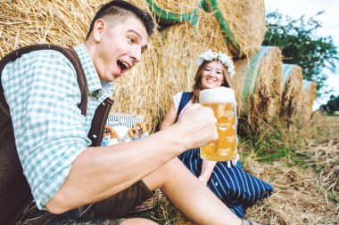 Saman balyalarının arkasında bira bardakları olan genç bir kadın ve adam. Oktoberfest kavramı