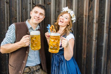 Bira bardakları ve tahta arka planda kraker olan genç bir kadın ve adam. Oktoberfest kavramı.