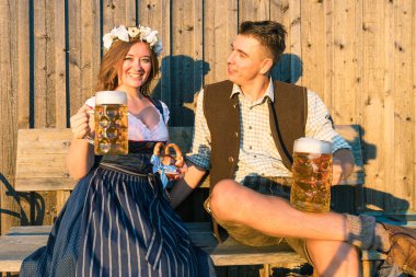 Bira bardakları ve tahta arka planda kraker olan genç bir kadın ve adam. Oktoberfest kavramı.
