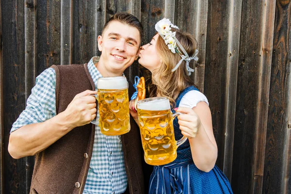 木製の背景にビールグラスとプレッツェルを持つ若い女性と男 オクトーバーフェストのコンセプト — ストック写真