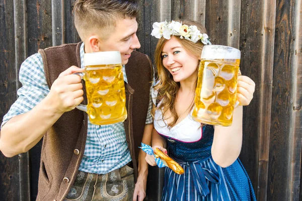 木製の背景にビールグラスとプレッツェルを持つ若い女性と男 オクトーバーフェストのコンセプト — ストック写真