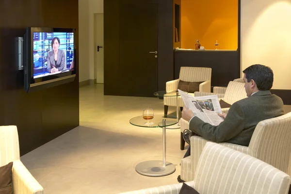 Man krant lezen en kijken naar Tv nieuws bij Hotel — Stockfoto