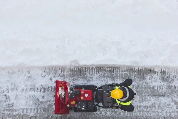 Worker cleaning snow on the sidewalk with a snowblower. Maintenance