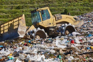Açık hava atık sahasında çöp öğüten ağır makineler. İsraf.