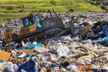 Açık hava atık sahasında çöp öğüten ağır makineler. İsraf.