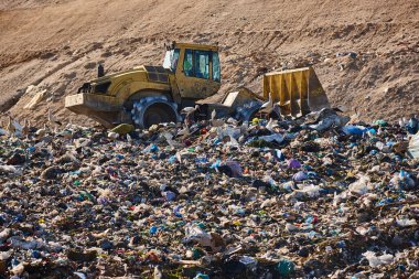 Heavy machinery shredding garbage in an open air landfill. Waste