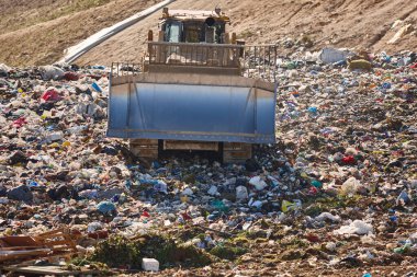 Açık hava atık sahasında çöp öğüten ağır makineler. İsraf.