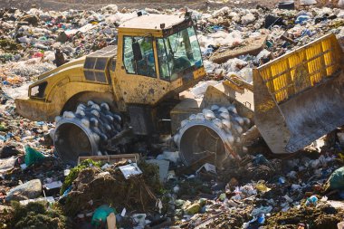 Heavy machinery shredding garbage in an open air landfill. Waste