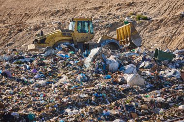 Heavy machinery shredding garbage in an open air landfill. Waste
