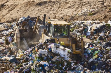 Açık hava atık sahasında çöp öğüten ağır makineler. İsraf.