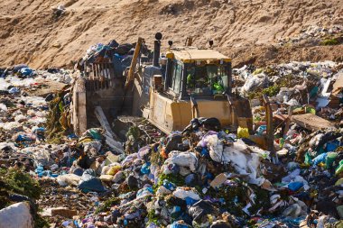 Açık hava atık sahasında çöp öğüten ağır makineler. İsraf.