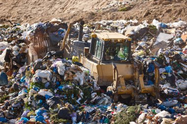 Açık hava atık sahasında çöp öğüten ağır makineler. İsraf.