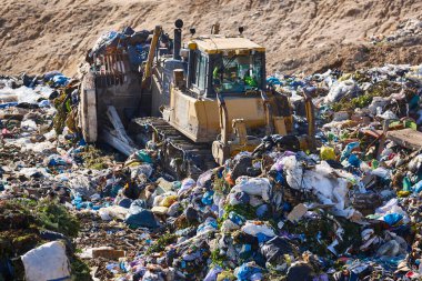 Açık hava atık sahasında çöp öğüten ağır makineler. İsraf.