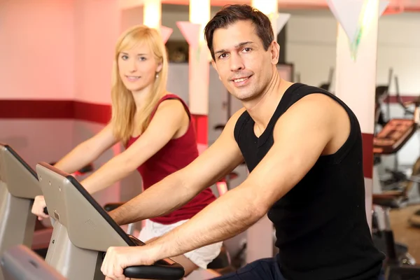 Atrakcyjna kobieta i mężczyzna, jazda na rowerze w siłowni — Zdjęcie stockowe