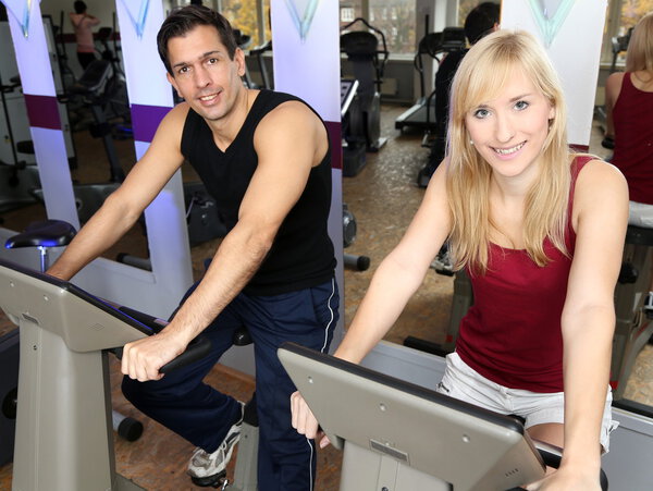 Attractive woman and a man cycling in a gym