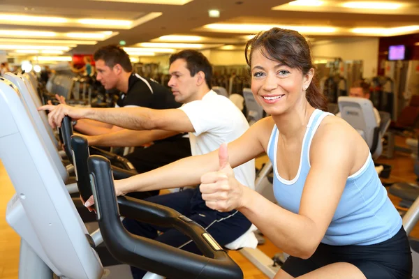 Dois homens e uma mulher em bicicleta de exercício mostrando os polegares para cima — Fotografia de Stock