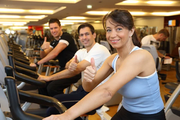 Dois homens e uma mulher em bicicleta de exercício mostrando os polegares para cima — Fotografia de Stock