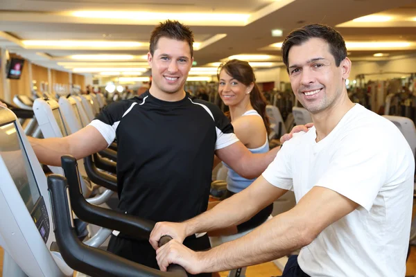 Três amigos em bicicletas de exercício em um ginásio — Fotografia de Stock