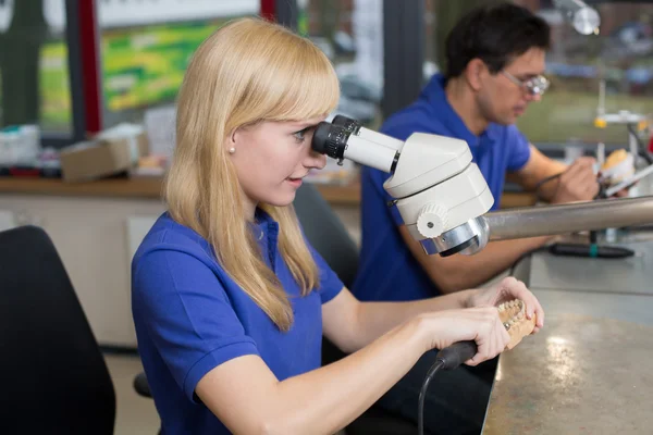 Técnico que trabalha em prótese dentária sob um microscópio — Fotografia de Stock