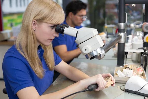 Technician working on dental prosthesis under a microscope — Stock Photo, Image